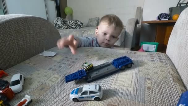 Маленький мальчик играет со своими игрушками на кресле. Малыш Тоддлер играет с игрушечными машинками . — стоковое видео