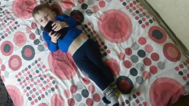 Ребенок лежит на кровати и смотрит на электронный смартфон дисплей — стоковое видео