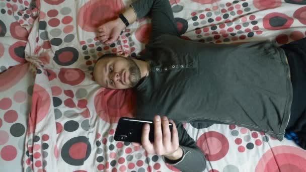 Joven usando smartphone en la cama por la mañana — Vídeo de stock