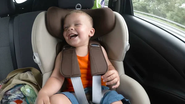 Baby boy in the childrens car seat in the car. Kid smiles, laughs and waves his hands happily. — Stock Photo, Image