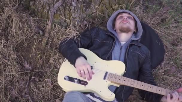 Hombre toca la guitarra eléctrica en un campo cerca del árbol al atardecer — Vídeo de stock