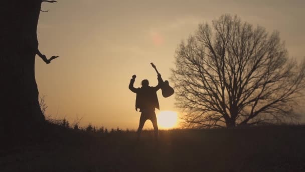 Silhouette des Gitarristen bei Sonnenuntergang in Zeitlupe. schwenkt seine Gitarre und seine Hand — Stockvideo