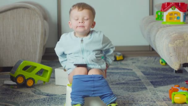 Adorable niño con un teléfono inteligente durante el entrenamiento de orinal en la habitación . — Vídeos de Stock