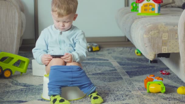 Adorable niño con un teléfono inteligente durante el entrenamiento de orinal en la habitación . — Vídeos de Stock