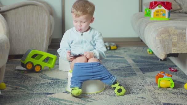 Adorable niño con un teléfono inteligente durante el entrenamiento de orinal en la habitación . — Vídeo de stock