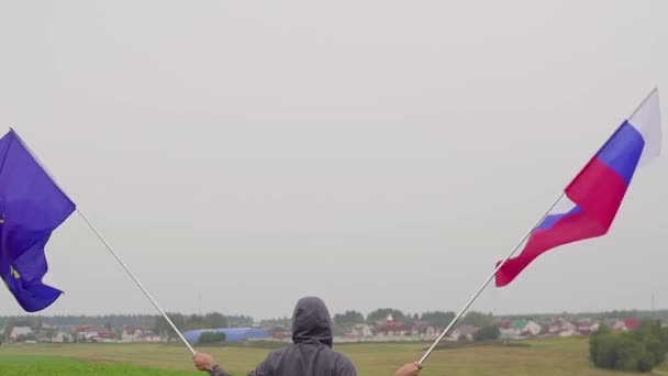 Video. Muž s vlajkami Evropské unie a Ruska na venkovská krajina. Pojem přátelství a usmíření. — Stock video