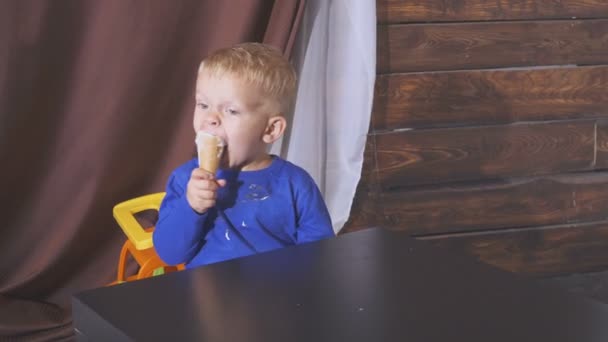Chłopiec jeść lody, siedząc na krzesełku. słodkie dzieci, ciesząc się lody w kształcie stożka wafel. spogląda w stronę. — Wideo stockowe