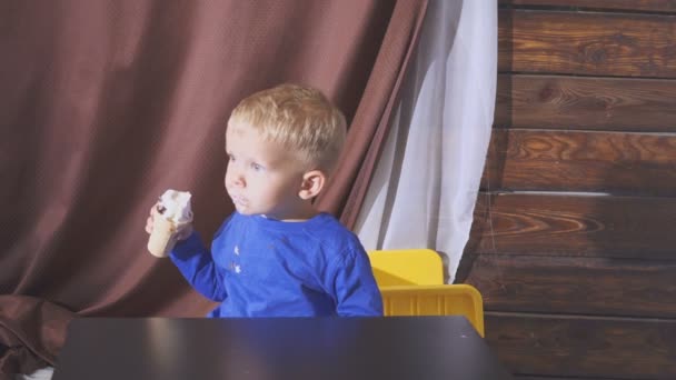 Jongen eten ijs zitten in een kinderstoel. schattig kind genieten van een ijsje in een wafel kegel. kijkt naar. — Stockvideo