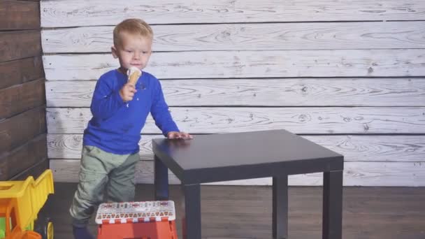 높은 자에 앉아 아이스크림을 먹고 소년. 와플 콘에 아이스크림을 즐기는 귀여운 아이. 쪽으로 보이는. — 비디오