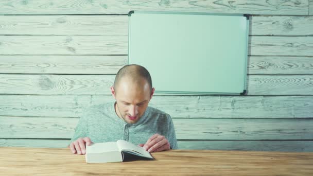 若いハンサムな男読書、カメラ、木製の板の背景で笑顔. — ストック動画