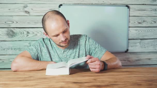 Молодий красивий чоловік читає книгу і посміхається на камеру, дерев'яні дошки фон . — стокове відео