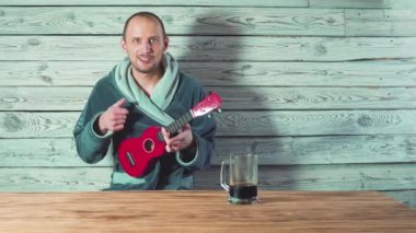 Bornozlu genç adam bira, şarkı ve ukulele arkadaşları için oynarken içiyor.