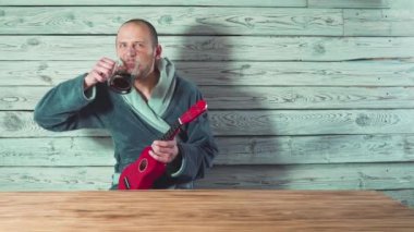 Bornozlu genç adam bira, şarkı ve ukulele arkadaşları için oynarken içiyor.