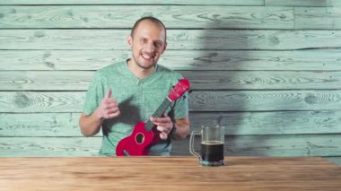 genç adam şarkı ve ukulele arkadaşları için oynarken bira içiyor.