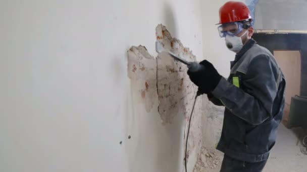 Trabajador en traje protector derriba la pared de yeso. Sucio, trabajo duro. Equipo de protección personal. Casco, respirador y gafas . — Vídeos de Stock