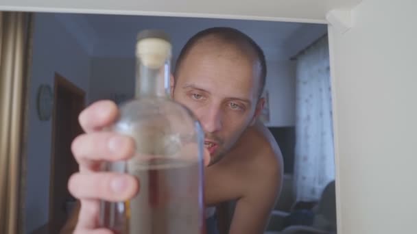 L'alcolizzato senza maglietta beve alcol da una bottiglia nell'armadio. triste a casa divano in abuso di alcol e alcolismo concetto . — Video Stock