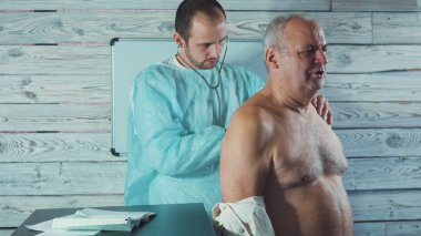 Klinikte kıdemli bir hastayla çalışan genç bir fizyoterapist. Ağrıyan kolun muayenesi.