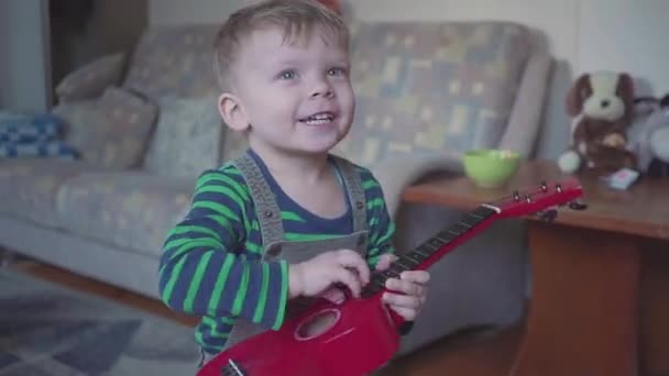 Веселий маленький хлопчик грає на гітарі співає і танцює — стокове відео