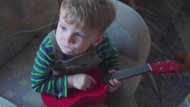 Fröhlicher kleiner Junge spielt Gitarre, singt und tanzt — Stockvideo