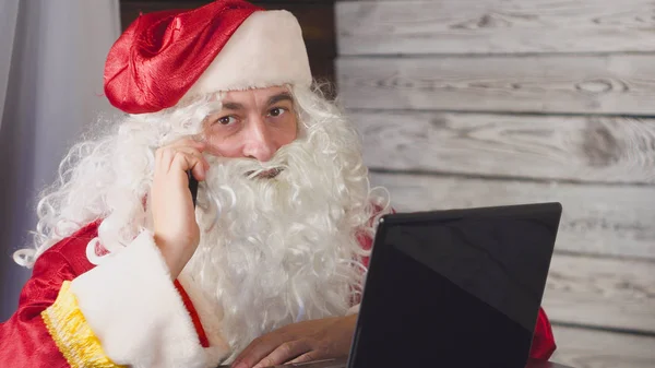 Weihnachtsmann mit Laptop im Büro. Weihnachtsmann mit Smartphone — Stockfoto