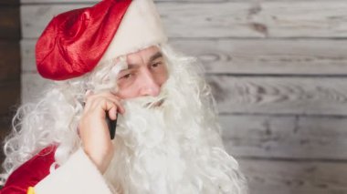 Noel Baba bir ofiste dizüstü bilgisayar ile çalışıyor. Noel Baba akıllı telefon kullanma