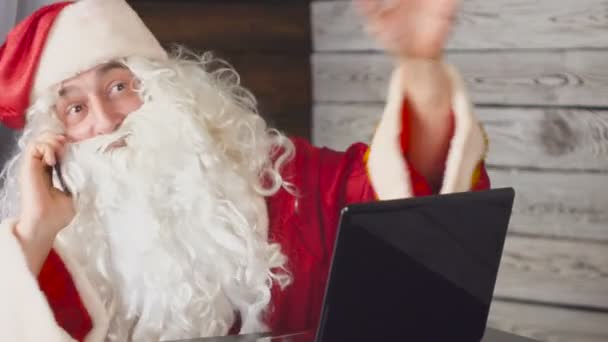 圣诞老人在办公室里用笔记本电脑工作。圣诞老人使用智能手机 — 图库视频影像
