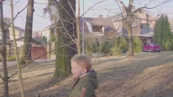 Ein Junge läuft durch den Wald in der Nähe von Privathäusern. Porträt eines glücklichen Jungen. Frühlings- oder Herbstabend. — Stockvideo