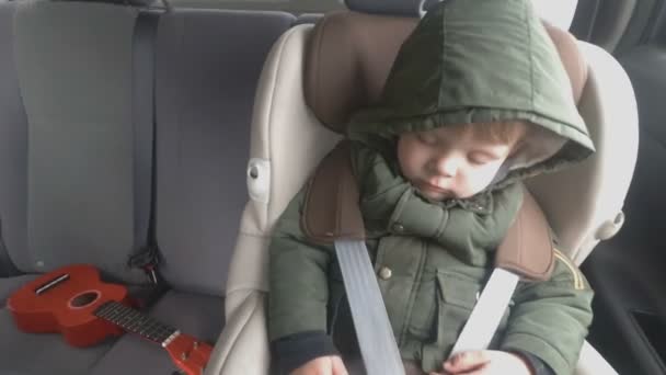 Ragazzino sul sedile posteriore di un'auto. La macchina sta andando su una brutta strada. Viaggia con il bambino. Bambino addormentato con una chitarra . — Video Stock