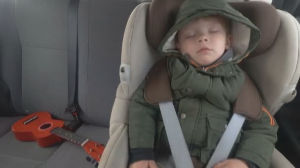 Kleine jongen op de achterbank van een auto. De auto gaat op een slechte weg. Reizen met baby. Sleeping Kid met een gitaar. — Stockvideo