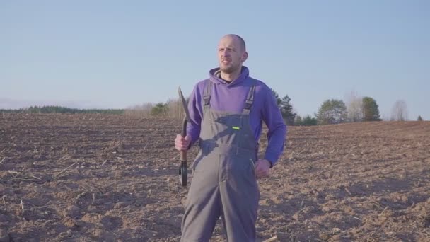Крупним планом портрет фермера, що стоїть на полі з лопатою в руках і дивиться на камеру . — стокове відео