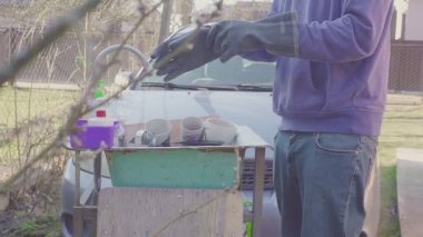 Genç adam dışarıda lavabonun yanında bulaşıkları yıkıyor. Eller soğuk sudan soğuktur. Eldivenli adam. Kamp tatilleri. Kavram