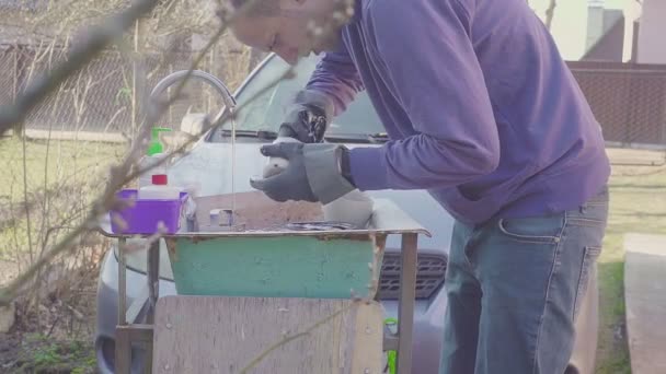 Young man washing dishes near the sink outside. Hands are cold from cold water. The man in gloves. Camping holidays. Concept — Stock Video