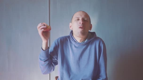 Unge man äter rött äpple hemma. Porträtt av en kille som äter ett färskt äpple och tittar på kameran. — Stockvideo