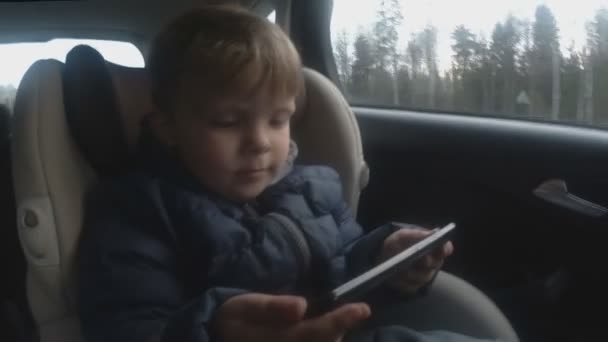 2 år baby dreng ved hjælp af telefon i bilen. blødt fokus – Stock-video