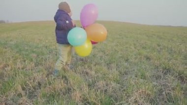Mutlu bebek çocuk, eğlenceli balonlar ile etrafında çalışan. Açık hava eğlencesi. Akşam gün batımında.