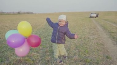 Küçük oğlu ile mutlu genç anne yürüyor ve seviniyor, oğlu elinde bir balon tutan.