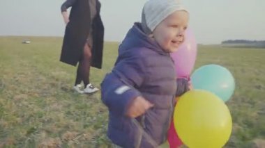 Küçük oğlu ile mutlu genç anne yürüyor ve seviniyor, oğlu elinde bir balon tutan.