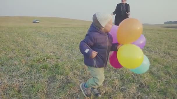 彼女の小さな息子と幸せな若い母親は歩いて喜んでいる、息子は手に風船を持って. — ストック動画