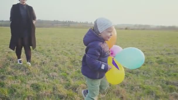 Щаслива молода мати з маленьким сином ходить і радіє, син тримає повітряні кулі в руці . — стокове відео