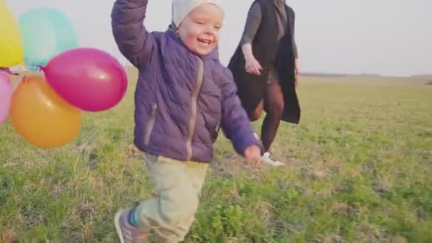Lycklig ung mamma med sin lille son går och jublar, son håller en ballonger i handen. — Stockvideo