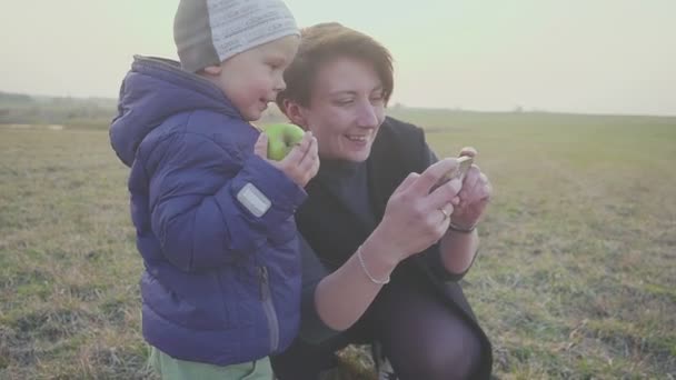 Familie moeder met haar kleine zoon het nemen van selfies in de avond buitenshuis. Poseren en glimlachen, genieten van de natuur. — Stockvideo