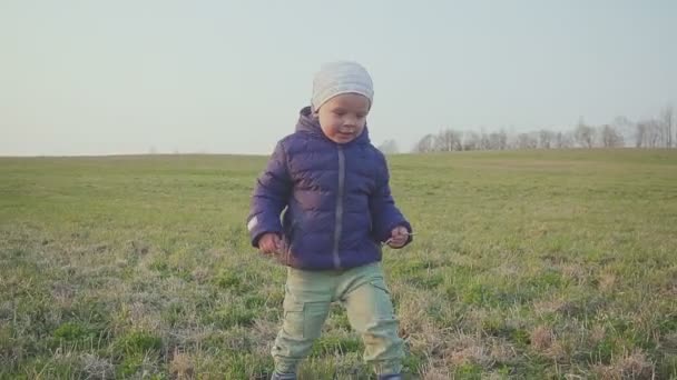 Kleine jongen rennen op het gras in het veld bij zonsondergang. — Stockvideo