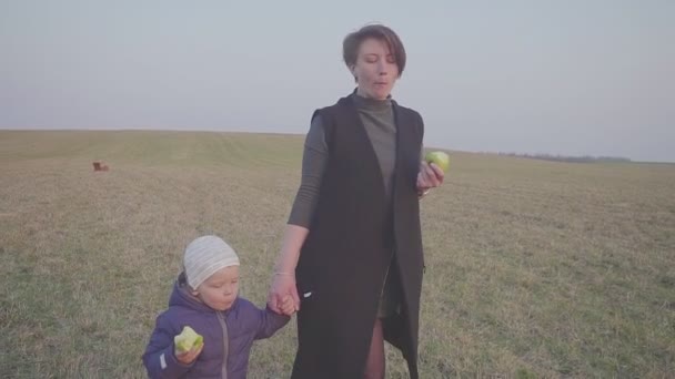 Madre e hijo comiendo una manzana en el paisaje exterior. Caminando por el campo y comiendo manzanas. Deja de viajar — Vídeos de Stock