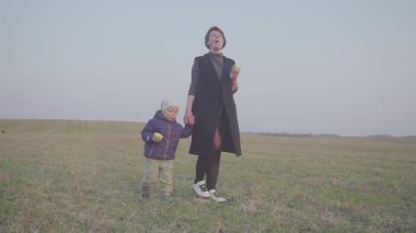Anne ve oğlu dış mekanda elma yiyor. Tarlada yürüyüp elma yemek. Seyahat etmeyi durdurun