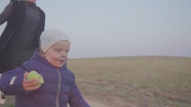 Anne ve oğlu dış mekanda elma yiyor. Tarlada koşup elma yiyor. Seyahat etmeyi durdurun