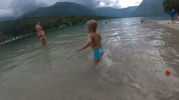 Niño pequeño 2 años en el agua del bosque lago de montaña. Vista desde atrás . — Vídeos de Stock