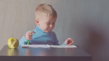 iki yaşındaki çocuk albümde marker ile çizim ve elma yiyor