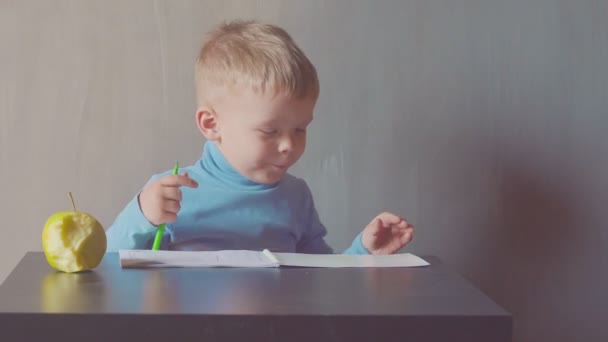 Två år gammal pojke ritar med markör på album och äta äpplen — Stockvideo
