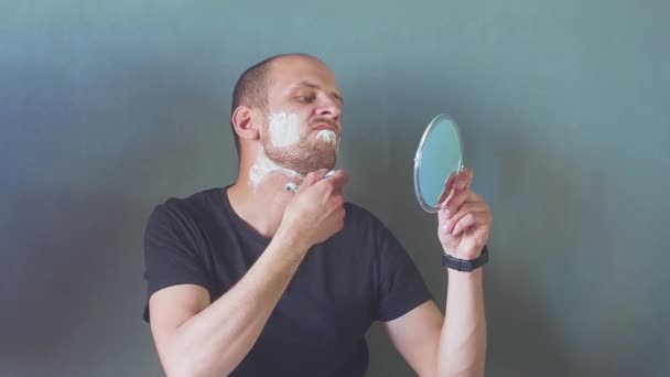 Мужчина бреет бороду с маленьким зеркалом в руках — стоковое видео