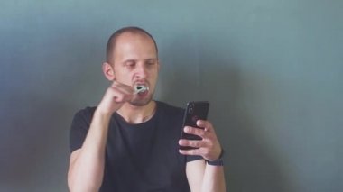 Akıllı telefon kullanan adama yaklaş. Telefon bağımlılığı kavramı. Genç iş adamı dişlerini fırçalarken telefonuyla sosyal medyayı karıştırıyor. Hd